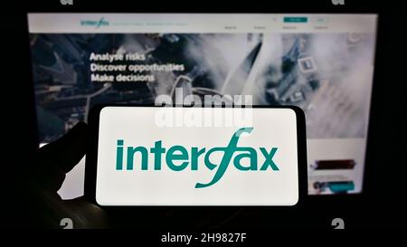 Persona che tiene uno smartphone con il logo dell'agenzia di stampa russa Interfax sullo schermo di fronte al sito web. Mettere a fuoco sul display del telefono. Foto Stock