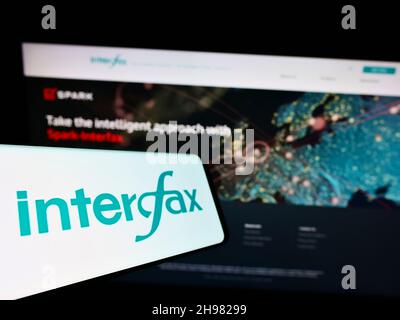 Telefono cellulare con logo dell'agenzia di stampa russa Interfax sullo schermo di fronte al sito web dell'azienda. Messa a fuoco al centro-sinistra del display del telefono. Foto Stock
