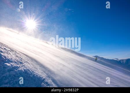 Ripida pista da sci e sole luminoso. Blizzard in superficie. Lo sciatore scende Foto Stock