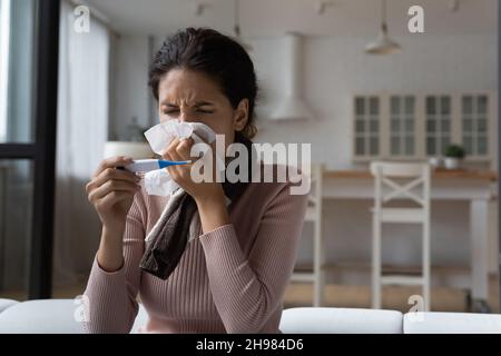 Primo piano donna malata che soffia il naso, con termometro digitale Foto Stock