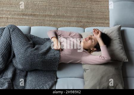 Vista dall'alto donna infelice che tocca la fronte, sdraiata solo sul divano Foto Stock