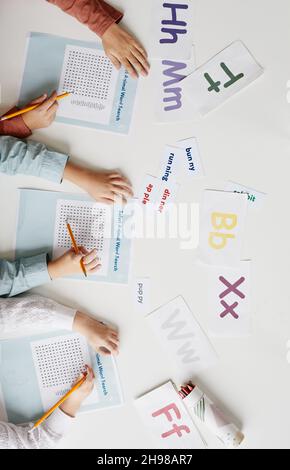 Vista ad alto angolo del gruppo di bambini seduti al tavolo con parole inglesi e facendo il compito su documenti Foto Stock