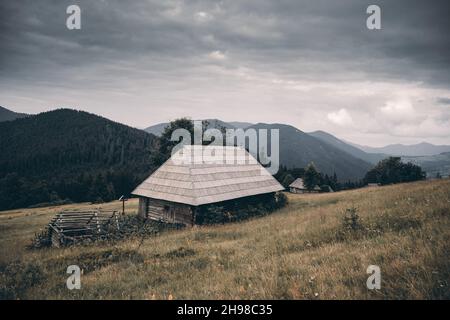 Pittoresco prato autunnale con vecchia casa in legno e cielo nuvoloso nelle montagne dei Carpazi, Ucraina. Fotografia di paesaggio Foto Stock