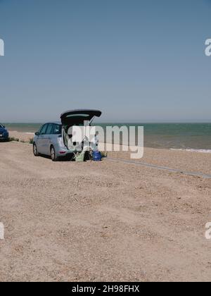 Un artista dipinge dal bagagliaio della loro auto con un cavalletto e tela sulla costa estiva del mare del Regno Unito - pittura ad aria plein - en plein air Foto Stock