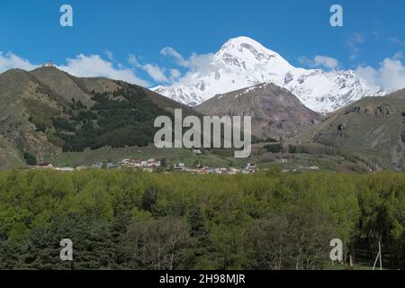 Domina il Monte Kazbek coperto di neve e la Chiesa della Trinità di Gergeti sulla sua collina sulla sinistra. Stepantsminda, regione di Mtskheta-Mtianeti, Georgia, Caucaso Foto Stock