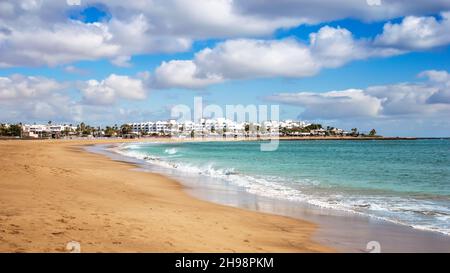 Vista sulla spiaggia di Playa de los Pocillos nella città di Puerto del Carmen, Lanzarote. Panorama di spiaggia sabbiosa con acque turchesi dell'oceano, case bianche di turisti Foto Stock