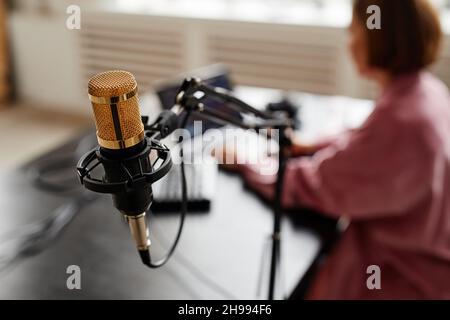 Primo piano del microfono da studio con il creatore femminile che imposta l'apparecchiatura di registrazione in background, spazio di copia Foto Stock