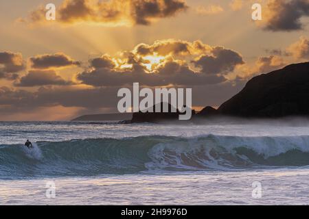 Surfista con un grande swell al tramonto sulla sempre popolare spiaggia di sabbia di Praa sulla costa sud della Cornovaglia Foto Stock