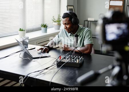 Ritratto del giovane uomo afroamericano che registra podcast in studio e utilizzando il portatile Foto Stock