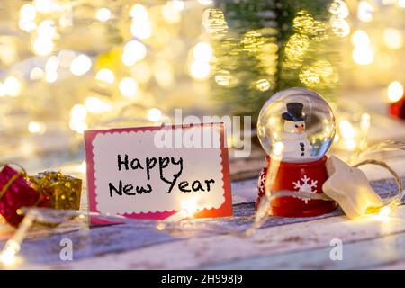 Felice anno nuovo scrivendo sul biglietto di auguri con decorazioni e luci Foto Stock
