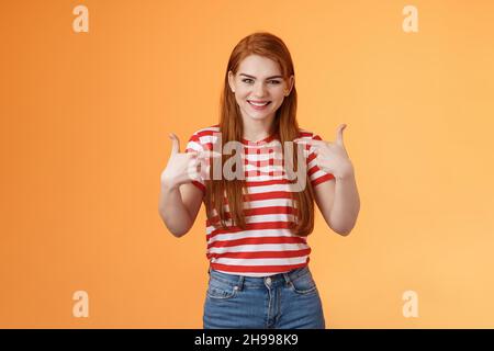 Bravissima ragazza motivata con redhead, che punta, indica le dita petto, bragging gioiosamente sorridente, chiacchierata con i propri successi, stand Foto Stock