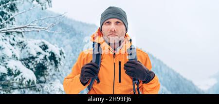 Giacca softshell arancione vestito da uomo con zaino, trekking lungo il percorso invernale delle montagne. Persone attive o sopravvivenza nel concetto di natura Foto Stock