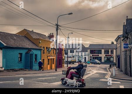 Signora disabile in scooter elettrico con cane guida che attraversa la strada. Arklow. Irlanda. Foto Stock