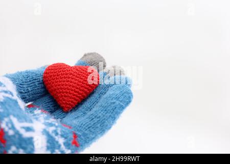 Cuore rosso sul palmo della mano in guanto caldo lavorato a maglia contro la neve bianca. Concetto di amore romantico, giorno di San Valentino o carità Foto Stock