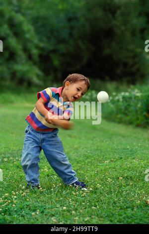 Giovane afghano-americano che colpisce con gioia un baseball con un pipistrello in un campo erboso, USA Foto Stock