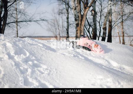 Scivoli per bambini. La ragazza ama la passeggiata invernale nella natura nella foresta, ha divertimento, gioca e si trova sulla neve Foto Stock