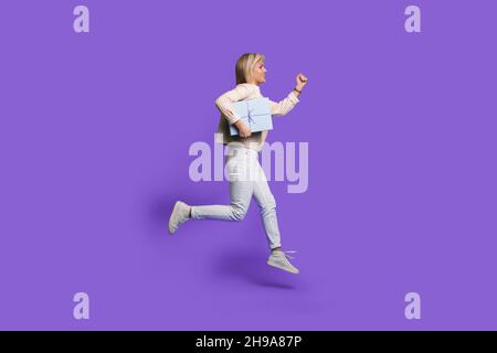 Foto di lato del profilo del corpo di una donna caucasica che salta su un regalo in corso, isolato su sfondo di colore viola Foto Stock