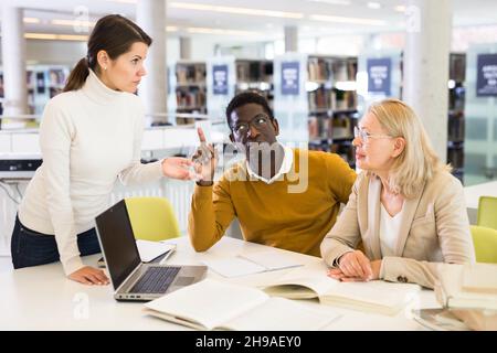 Tutor femminile che aiuta gli studenti a prepararsi per l'esame in biblioteca Foto Stock