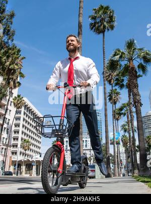 Il ragazzo felice in formalwear guida scooter elettrico sul marciapiede, scooting Foto Stock