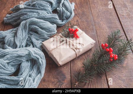 Confezione regalo in carta artigianale con fondo in tovaglia grigio garza. Trama, sfondo, motivo. Rami di abete e bacche rosse come decorazione Foto Stock