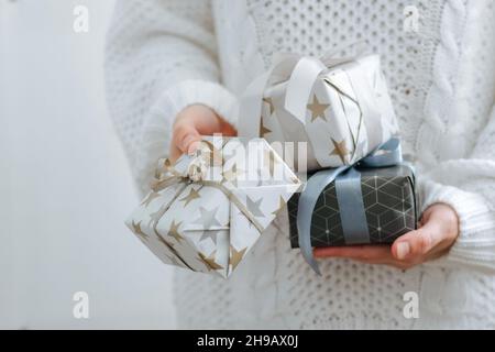 Una ragazza in maglione bianco contiene regali di festa. Le mani femminili stanno tenendo le scatole di festa. Il concetto di preparazione delle vacanze Foto Stock