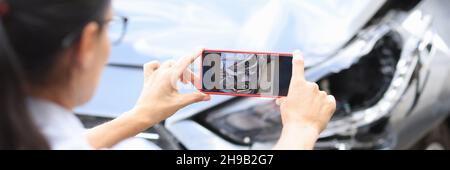 L'agente donna scatta foto dei danni all'auto dopo un incidente dallo smartphone Foto Stock