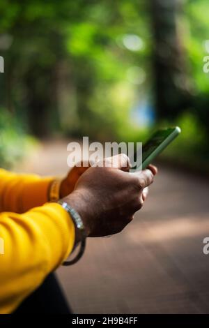 una persona che utilizza uno smartphone su sfondo verde bokeh, una mano maschio che tiene uno smartphone Foto Stock