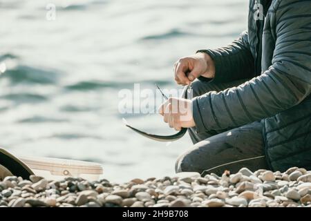 Primo piano delle mani del pescatore che prende il granaio catturato dal gancio. L'uomo hobby pesca sul mare stringe una bobina di lenza di pesce estate. Calma Foto Stock