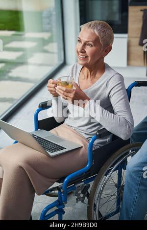 Utente in sedia a rotelle anziano che si gode il suo tè alle erbe Foto Stock