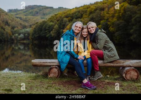 Bambina con madre e nonna seduta su panca e guardando la macchina fotografica outoors vicino al lago. Foto Stock