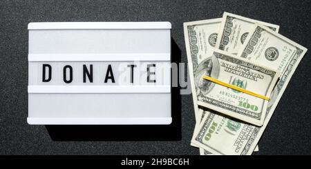 Cartone luminoso con parole DONATE in lettere nere intorno alle banconote in dollari USA. Soldi, affari, finanza, investimento, risparmio Foto Stock