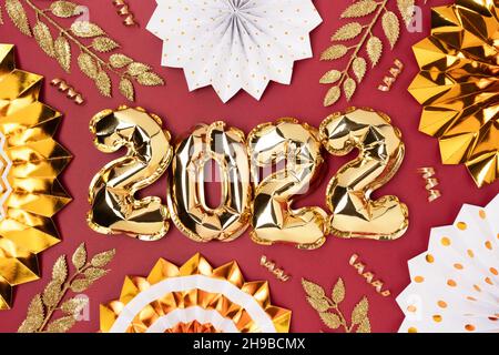 2022 palloncini gonfiabili d'oro e decorazioni scintillanti su sfondo rosso. Il concetto di Capodanno. Foto Stock