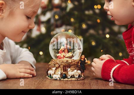 Bambini che guardano una palla di vetro con una scena della nascita di Gesù Cristo Foto Stock