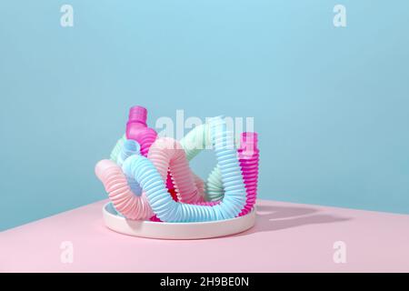 Tubo curvo rosa, blu, menta, antistress pop su piastra bianca con ombra su sfondo rosa. Giocattolo per bambini luminoso. Foto Stock
