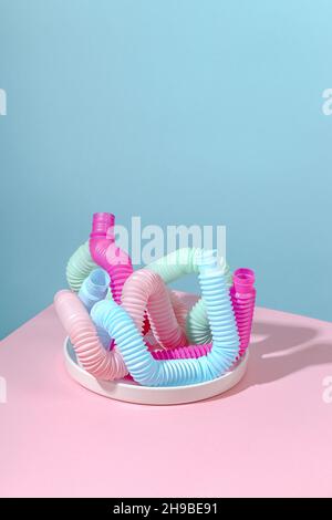 Tubo curvo rosa, blu, menta, antistress pop su piastra bianca con ombra su sfondo rosa. Giocattolo per bambini luminoso. Foto Stock