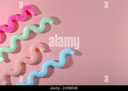 Giocattolo curvo rosa blu menta antistress pop tube con ombra su sfondo rosa. Giocattolo per bambini luminoso. CopySpace Foto Stock