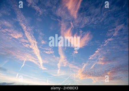 Formazioni di nubi spesse e percorsi di condensazione dall'aereo con il sole mattutino che illumina le nuvole e contrasta con una tinta arancione. Foto Stock