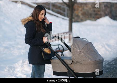 Giovane madre che cammina con il suo bambino in pram. Bellissimo stoller. Fotosessione invernale Foto Stock