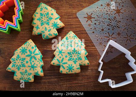 Biscotti a forma di albero di Natale con motivo fiocchi di neve, stencil e taglierine biscotti su un tagliere di legno Foto Stock