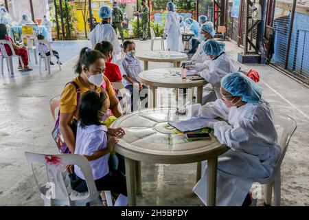 Quezon City, Filippine. 6 dicembre 2021. Gli studenti che indossano le maschere protettive sono assistiti dai loro genitori mentre subiscono un test volontario dell'antigene COVID-19 prima di frequentare una classe faccia a faccia presso una scuola elementare a Quezon City, nelle Filippine, 6 dicembre 2021. Alcune scuole selezionate nelle Filippine lunedì hanno iniziato la corsa di pilota delle classi faccia a faccia limitate mentre il paese continua a registrare i casi declinanti di COVID-19. Credit: Rouelle Umali/Xinhua/Alamy Live News Foto Stock