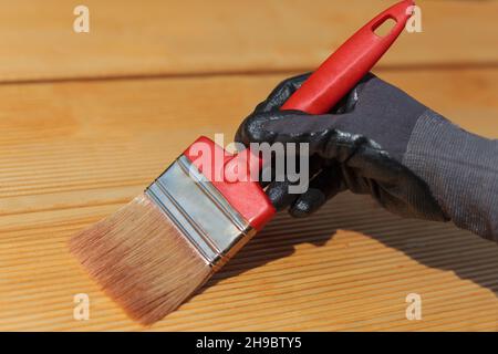 Applicazione della vernice protettiva sui pannelli di legno. Spazzola rossa e olio per terrazze per terrazze in legno. Foto Stock