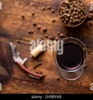 Bicchiere con vino rosso e chicchi di caffè su un vecchio sfondo di legno marrone. Foto Stock