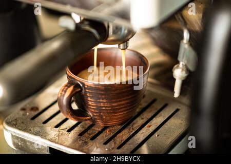 Il caffè viene preparato in una macchina da caffè. Il caffè appena fatto viene versato in una tazza di terracotta. Foto Stock