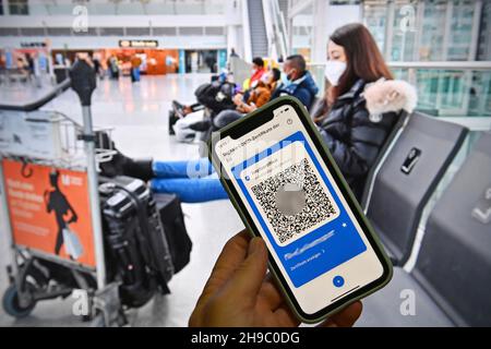 Foto topica/simbolo: Certificati digitali del Covid dell'UE su smartphone, protezione completa della vaccinazione, certificato di vaccinazione, tessera di vaccinazione digitale, tessera di vaccinazione. Giovane donna con maschera facciale, maschera con valigia, bagaglio all'aeroporto di Monaco il 6 dicembre 2020. Seduto al terminal, sala partenze, in attesa di partenza e guardando il suo smartphone. MODELLO RILASCIATO! Foto Stock