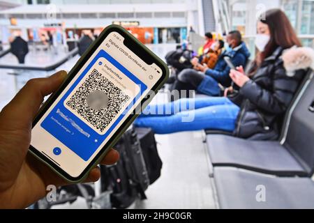 Foto topica/simbolo: Certificati digitali del Covid dell'UE su smartphone, protezione completa della vaccinazione, certificato di vaccinazione, tessera di vaccinazione digitale, tessera di vaccinazione. Giovane donna con maschera facciale, maschera con valigia, bagaglio all'aeroporto di Monaco il 6 dicembre 2020. Seduto al terminal, sala partenze, in attesa di partenza e guardando il suo smartphone. MODELLO RILASCIATO! Foto Stock