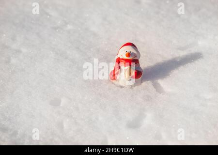 Il giocattolo pupazzo di neve si trova sulla copertura della neve nella soleggiata serata invernale al tramonto. Sfondo di neve minimalista con pupazzo di neve Foto Stock