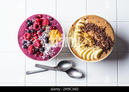 Ciotole di frullato al cioccolato e alla bacca su sfondo piastrellato bianco, vista dall'alto. Concetto di cibo vegano crudo. Foto Stock