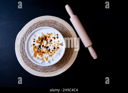 Ravioli manti turchi su piatto bianco con salsa di menta al pepe rosso accanto al matterello può essere isolato su sfondo nero, manti idea Concept Foto Stock