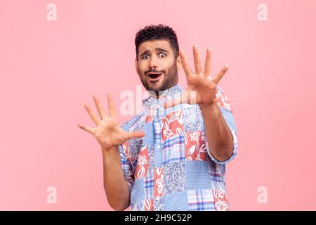 Temo. Ritratto di uomo sconvolto e spaventato in camicia blu casual stile urlando in orrore e paura, mantenendo le mani sollevate per difendersi. Studio interno girato isolato su sfondo rosa. Foto Stock