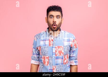 Ritratto di uomo divertente eccitato in blu camicia casual stile con labbra di pout e grandi occhi stupiti, guardando sorpreso e sciocco alla macchina fotografica, si è chiesto espressione. Studio interno girato isolato su sfondo rosa. Foto Stock